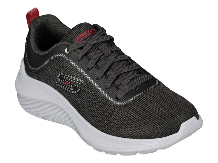 Tenis Skechers color gris con suela blanca y pequeña pestaña roja en el talón.