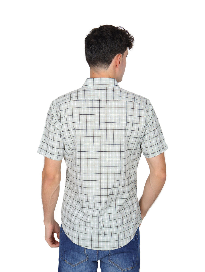 Hombre vistiendo una camisa blanca de manga corta con estampado de cuadros negros y pantalones jeans azules.