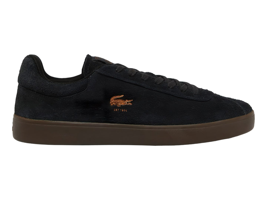 Tenis Lacoste de gamuza color negro con suela café y logotipo dorado en el lateral.