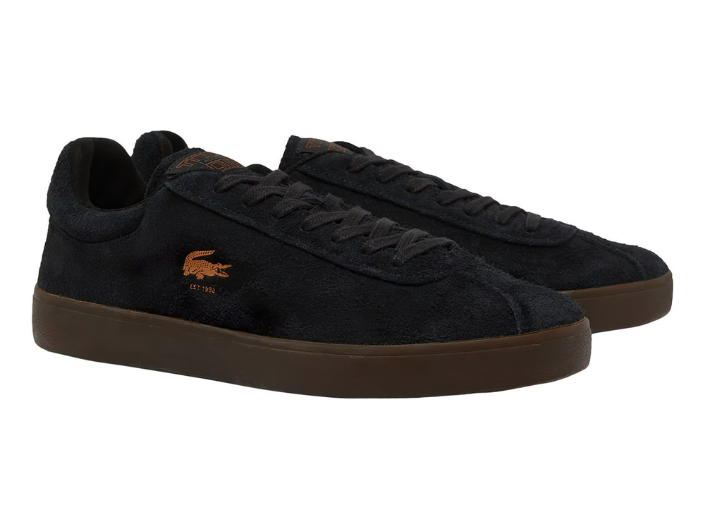 Tenis Lacoste de gamuza color negro con suela café y logotipo dorado en el lateral.