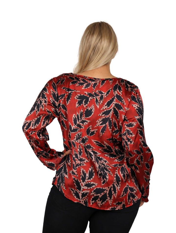 Mujer vistiendo una blusa roja con estampado de hojas negras y manga larga.