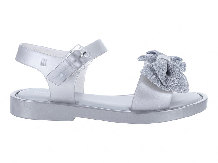 Sandalia plateada para niña con moño decorativo y correa ajustable.