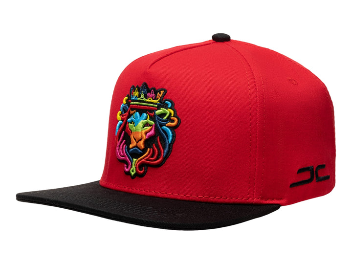 Gorra snapback roja con visera plana negra y bordado colorido de un león con corona en el frente.