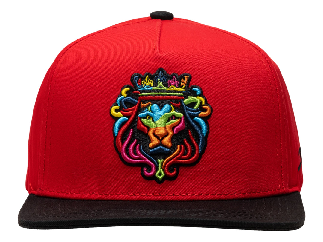 Gorra snapback roja con visera plana negra y bordado colorido de un león con corona en el frente.