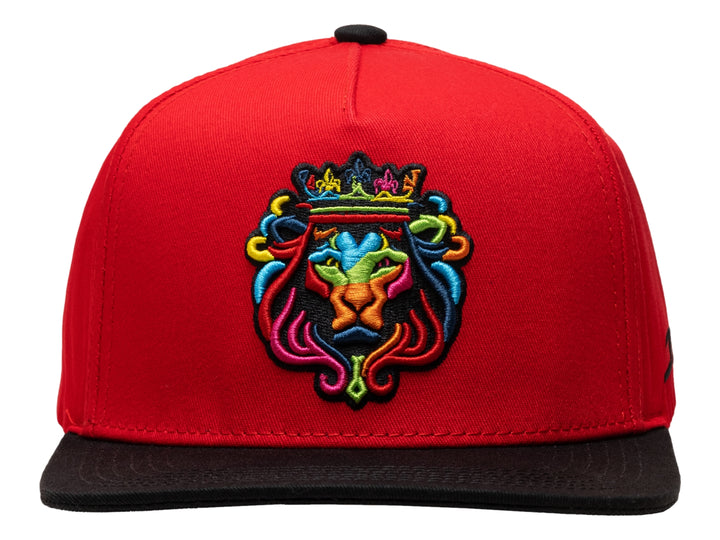 Gorra snapback roja con visera plana negra y bordado colorido de un león con corona en el frente.