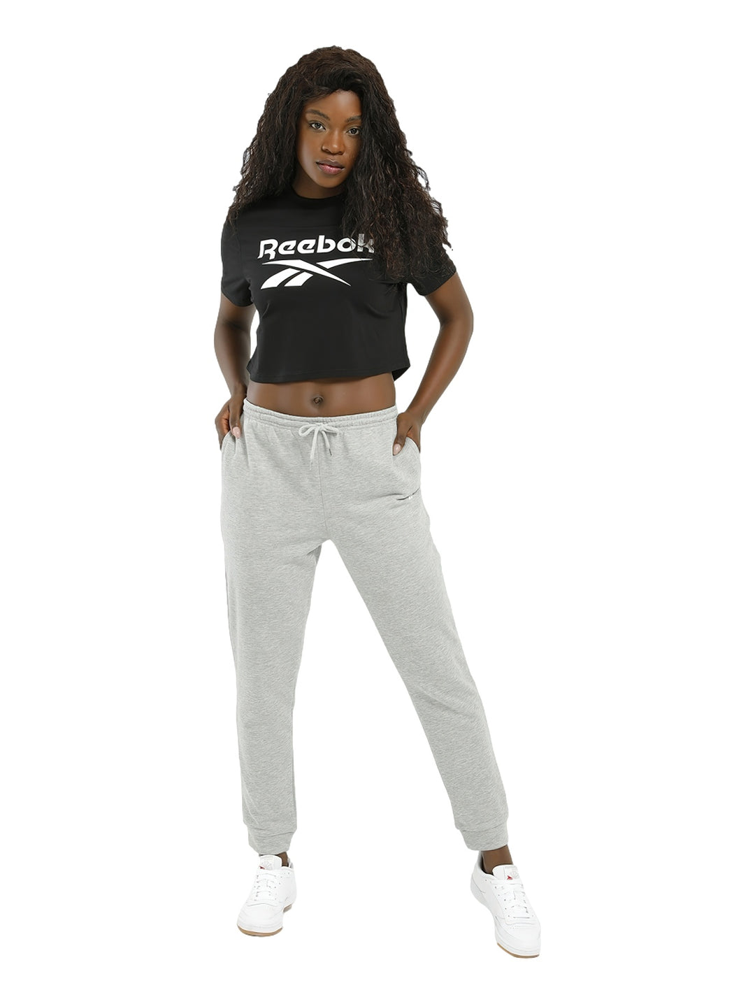 Mujer vistiendo una camiseta crop top negra de Reebok con logotipo blanco grande en el pecho.