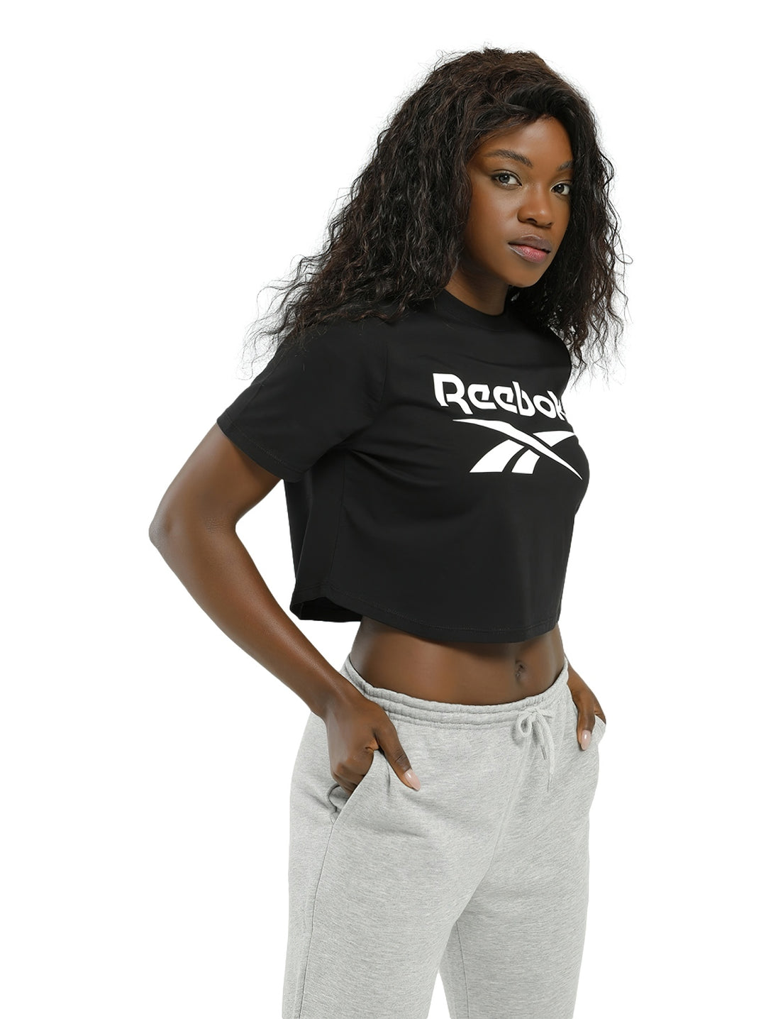 Mujer vistiendo una camiseta crop top negra de Reebok con logotipo blanco grande en el pecho.