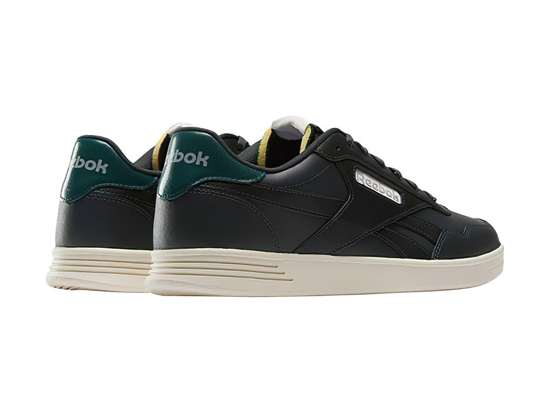 Tenis Reebok Court Advance color gris oscuro con detalle verde en el talón y suela blanca.