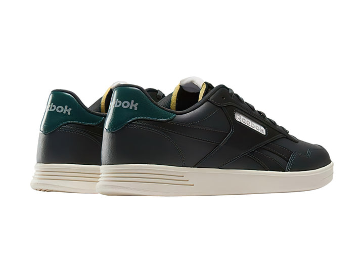 Tenis Reebok Court Advance color gris oscuro con detalle verde en el talón y suela blanca.