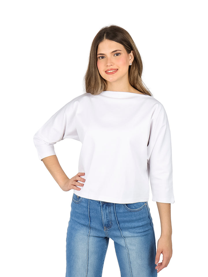 Mujer vistiendo una blusa blanca de manga larga con escote ojal y pantalones de mezclilla azules.