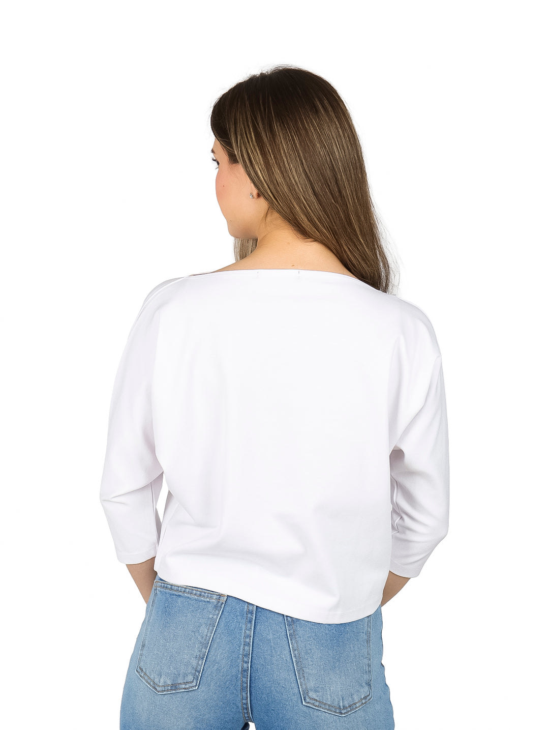 Mujer vistiendo una blusa blanca de manga larga con escote ojal y pantalones de mezclilla azules.
