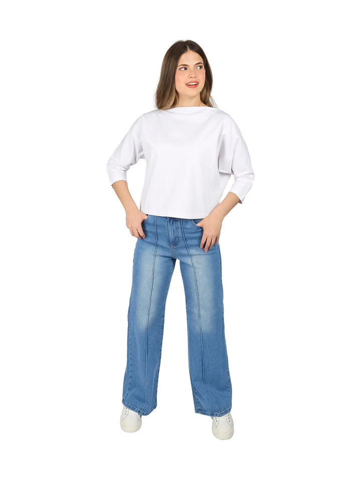Mujer vistiendo una blusa blanca de manga larga con escote ojal y pantalones de mezclilla azules.
