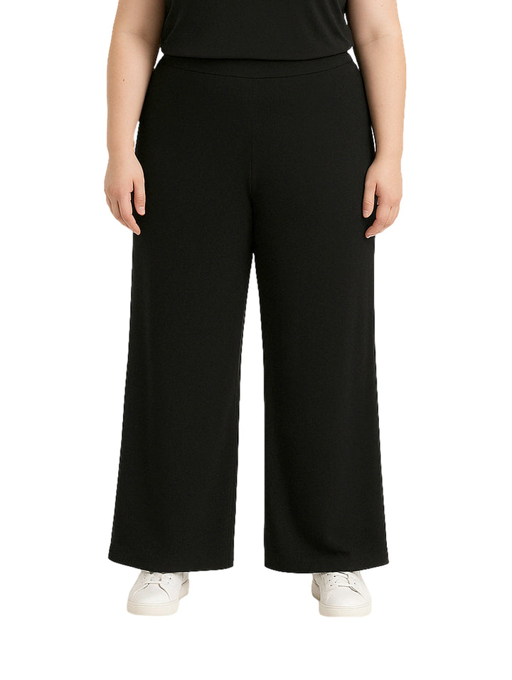 Mujer vistiendo pantalón recto ancho de color negro con pretina elástica y tenis blancos.