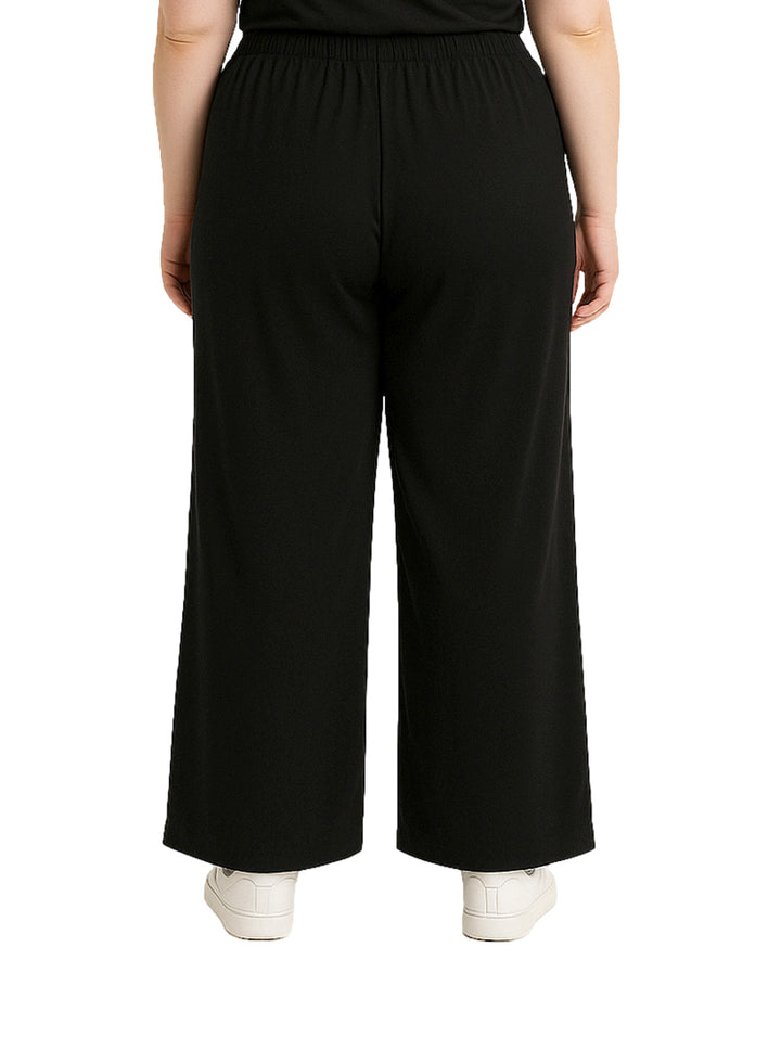 Mujer vistiendo pantalón recto ancho de color negro con pretina elástica y tenis blancos.