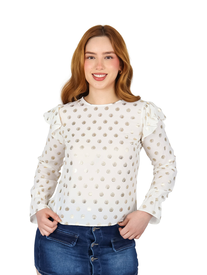 Mujer vistiendo blusa color ivory con estampado de puntos dorados, manga larga y detalle de volantes en los hombros.