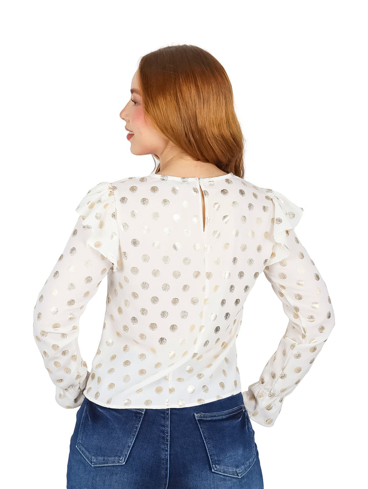 Mujer vistiendo blusa color ivory con estampado de puntos dorados, manga larga y detalle de volantes en los hombros.