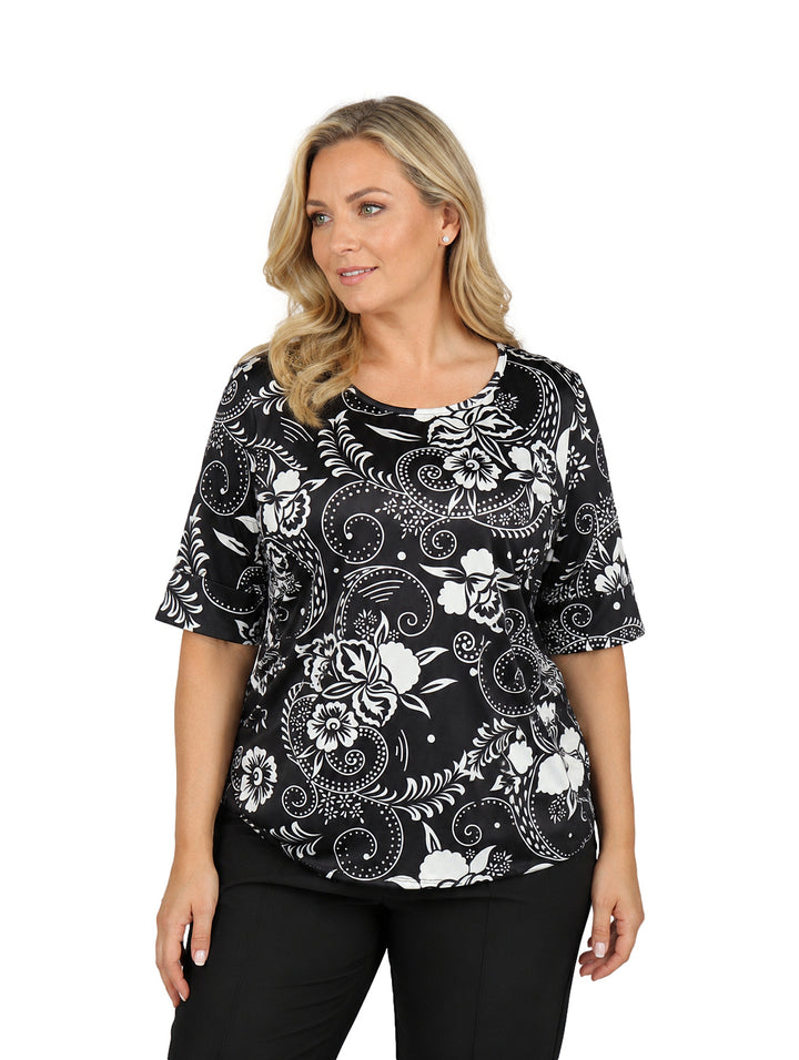 Mujer vistiendo blusa de manga corta color negro con estampado floral blanco y cuello redondo.