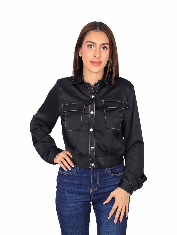 Mujer vistiendo camisa negra de manga larga con botones metálicos y bolsillos con costuras blancas.