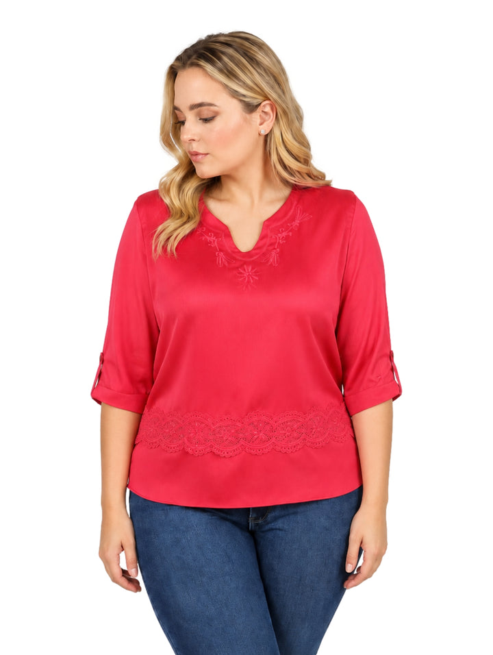 Mujer vistiendo blusa rosa de manga corta con detalles de encaje y pantalones vaqueros azules.