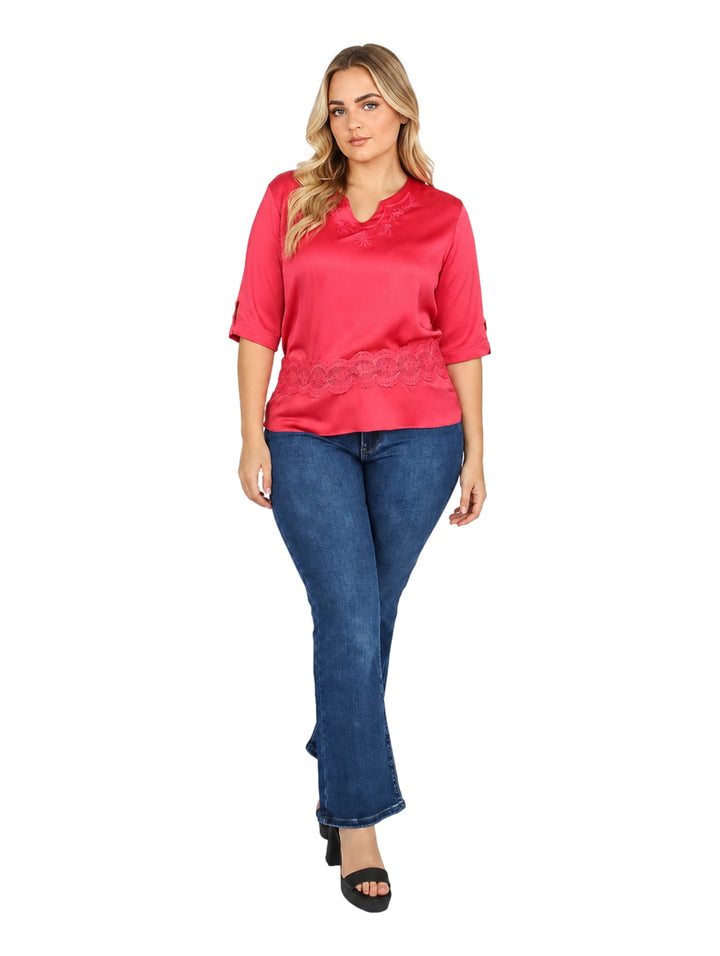 Mujer vistiendo blusa rosa de manga corta con detalles de encaje y pantalones vaqueros azules.