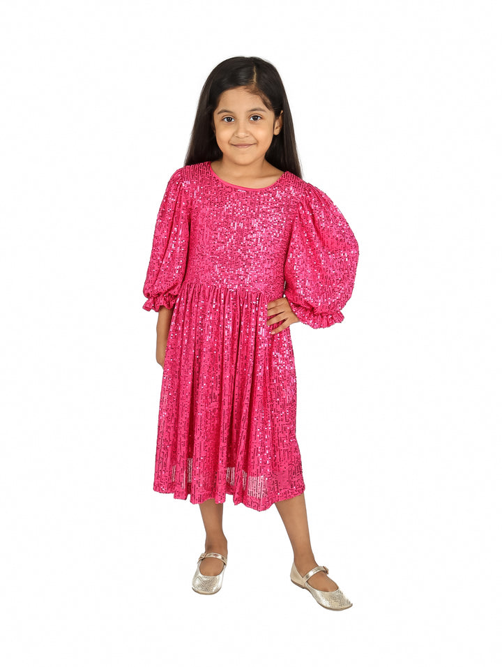 Niña vistiendo un vestido color fucsia brillante con lentejuelas y mangas abullonadas.