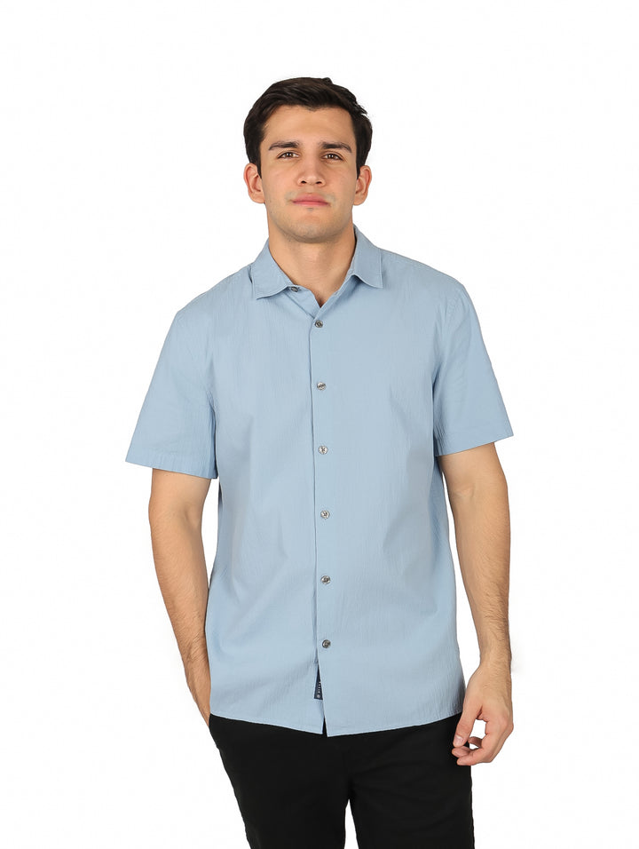 Hombre vistiendo una camisa de manga corta color azul claro con botones y cuello.