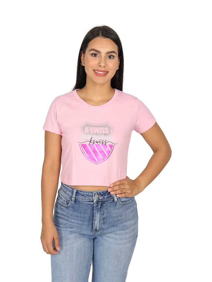 Mujer vistiendo playera rosa de manga corta con logo de K-SWISS en el pecho y pantalones mezclilla azules.