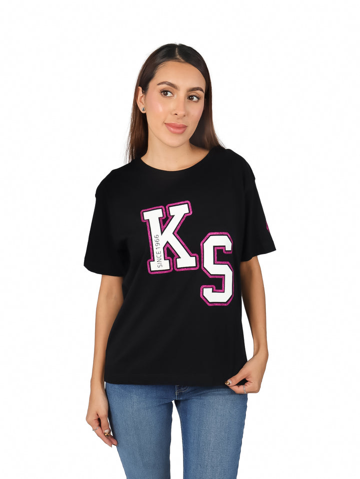 Mujer vistiendo playera negra de manga corta K-SWISS con logotipo KS en blanco y rosa.
