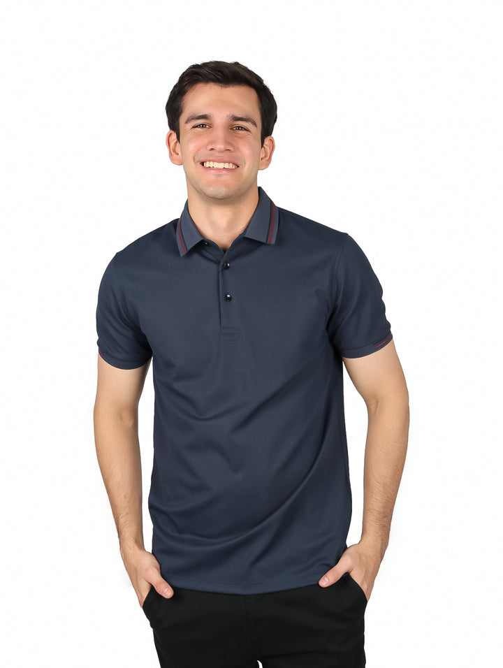 Hombre vistiendo playera polo color verde oscuro con detalles rojos en el cuello y mangas.