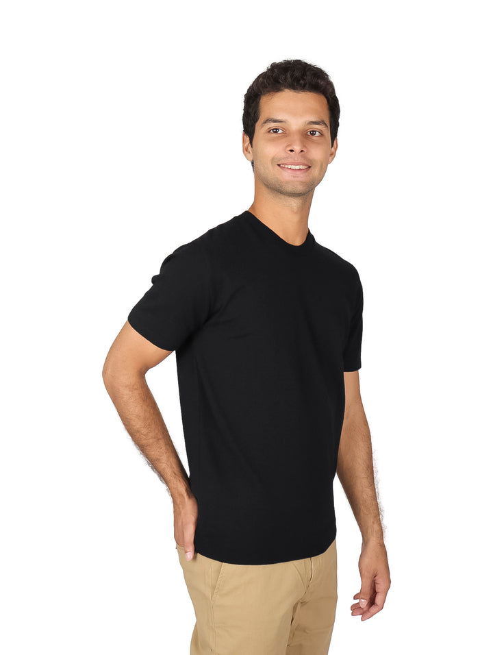 Hombre vistiendo una playera tejida lisa de color negro con cuello redondo y manga corta.