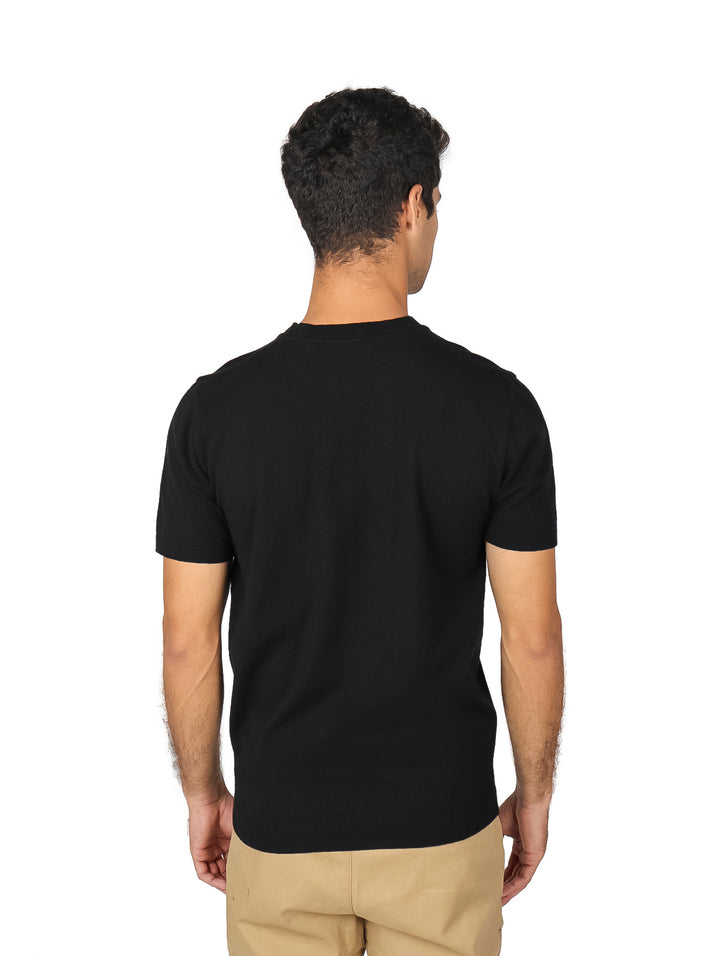 Hombre vistiendo una playera tejida lisa de color negro con cuello redondo y manga corta.