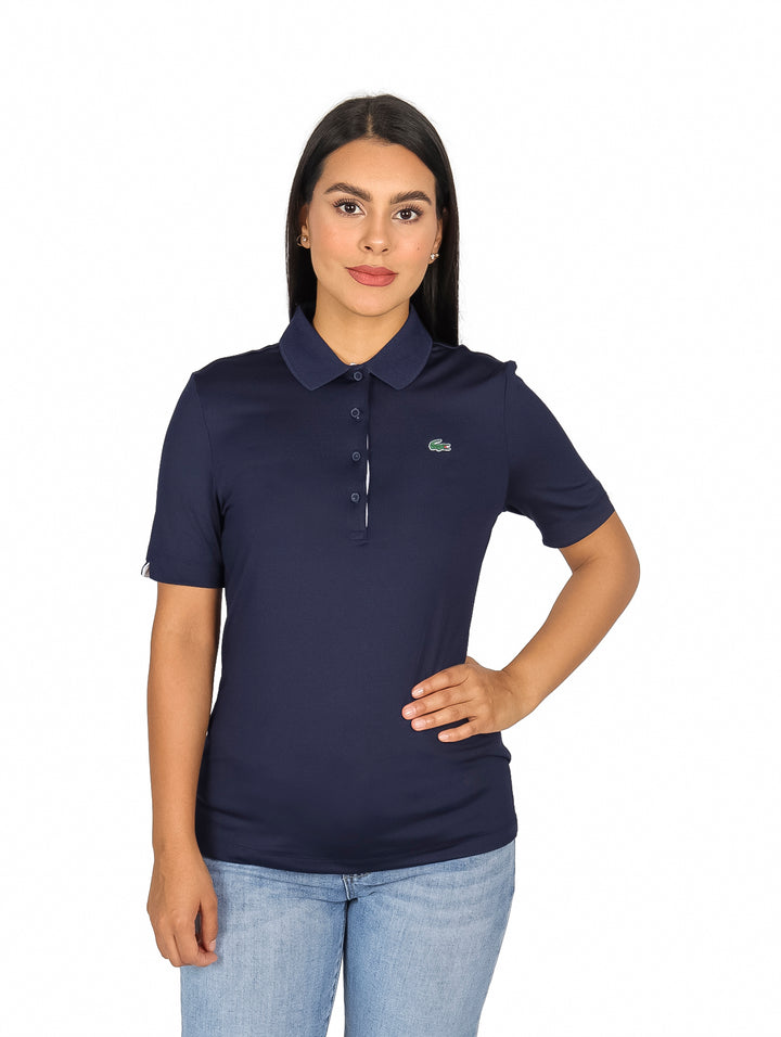 Mujer vistiendo polo azul marino de manga corta con cuello y logo de Lacoste.