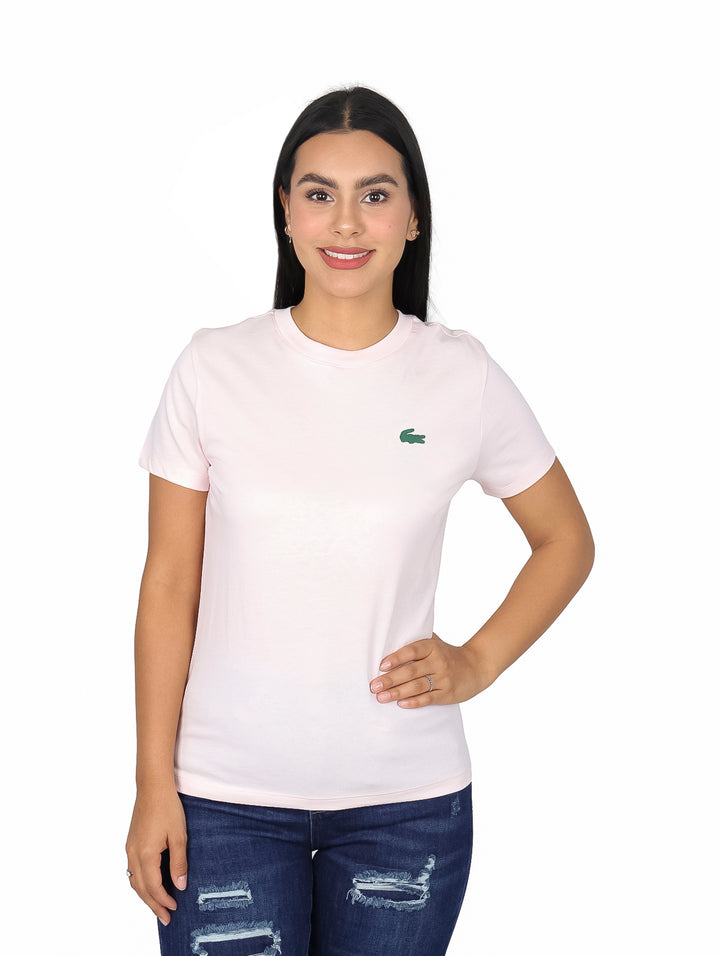 Mujer vistiendo una playera rosa claro de manga corta marca Lacoste y jeans azules.