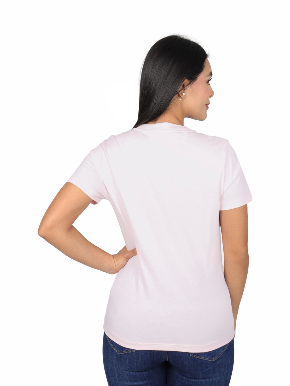 Mujer vistiendo una playera rosa claro de manga corta marca Lacoste y jeans azules.