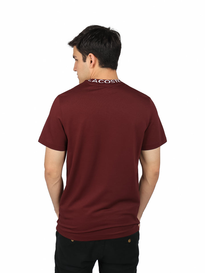 Hombre vistiendo camiseta Lacoste color expresso con banda blanca en el cuello y logotipo en el pecho.