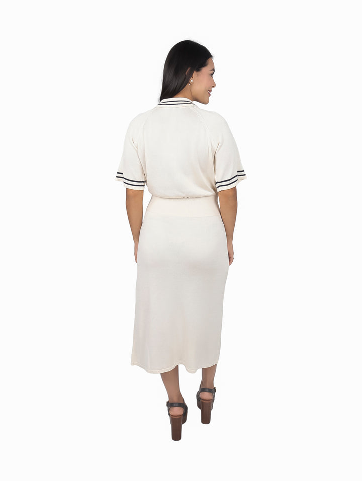 Mujer vistiendo un vestido polo midi color blanco hueso con detalles negros en las mangas.