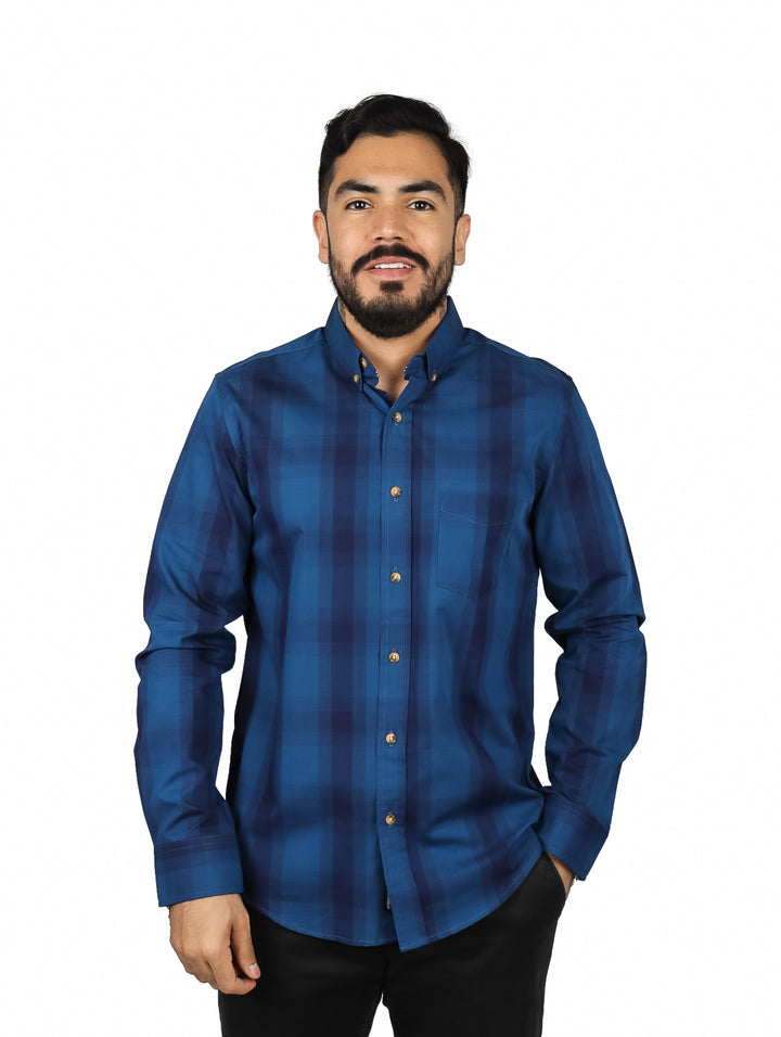 Hombre vistiendo una camisa de manga larga color azul con estampado de cuadros y botones frontales.