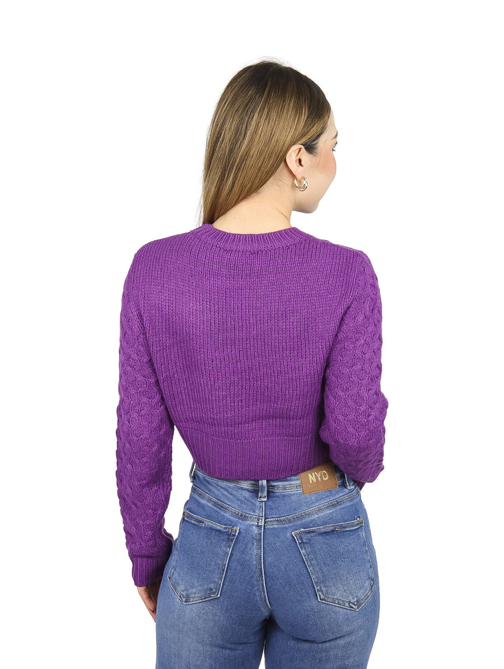 Mujer vistiendo un suéter corto tejido de color lila con cuello redondo y manga larga.