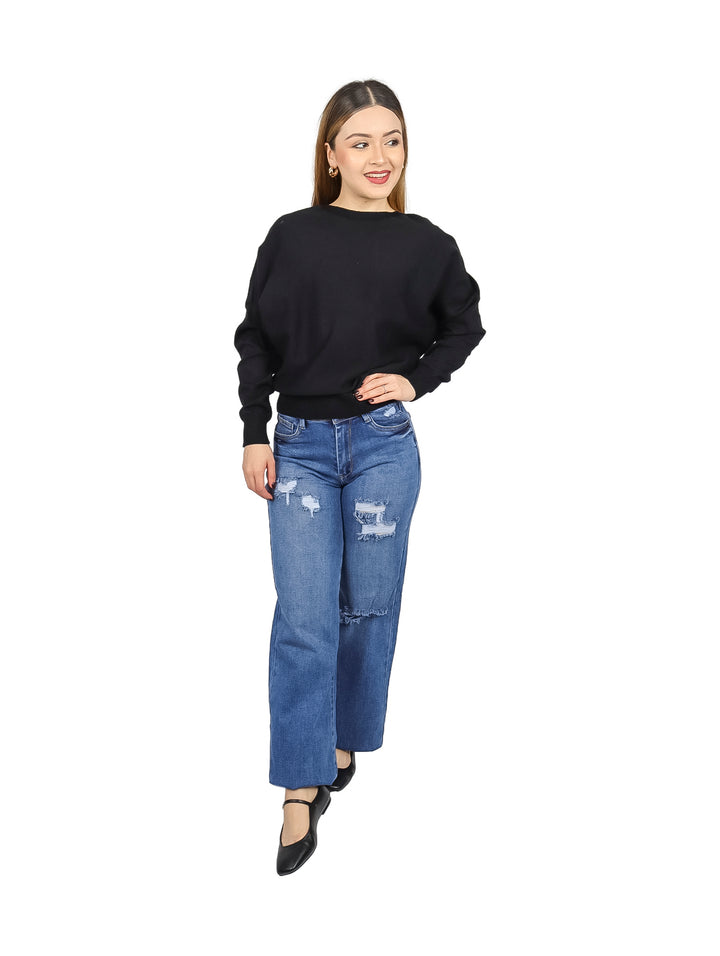 Mujer vistiendo un suéter ancho de color negro y pantalones mezclilla azules.