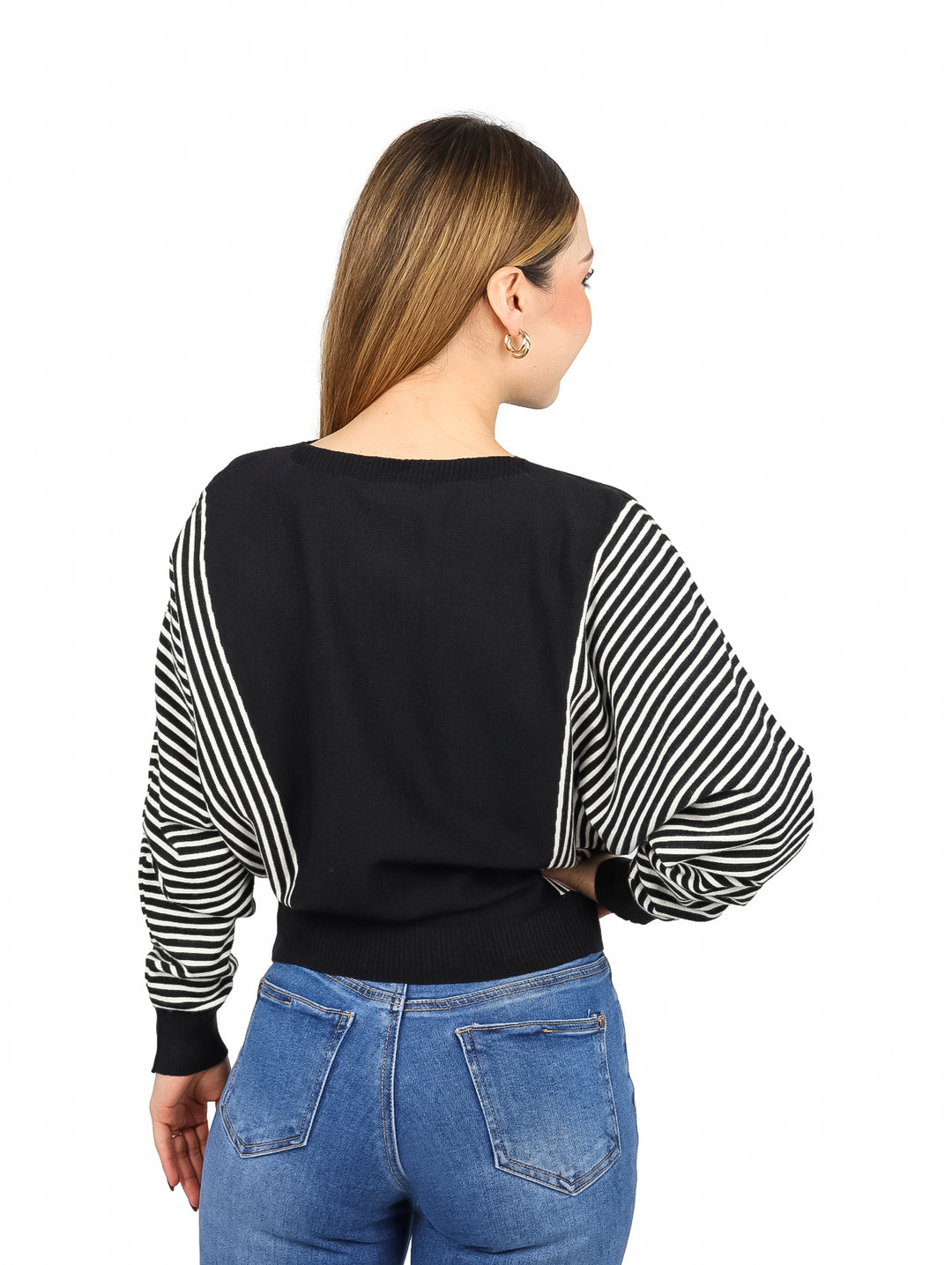 Mujer vistiendo un suéter negro con mangas a rayas blancas y negras y jeans azules.