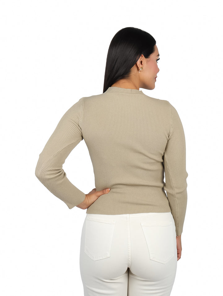 Mujer vistiendo suéter color camel de manga larga con escote en el pecho y pantalones blancos.