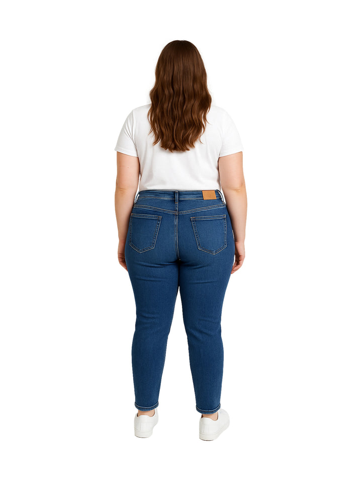 Mujer vistiendo pantalones jeans skinny en color azul oscuro con playera blanca y tenis blancos.