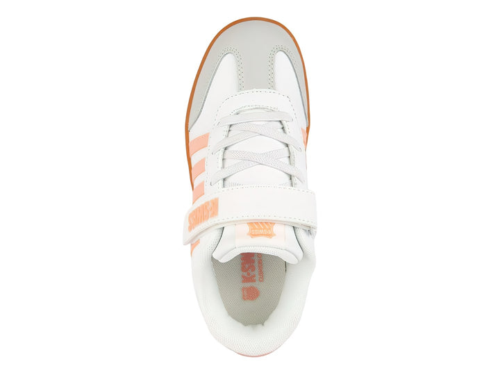 Tenis blancos K-Swiss con rayas rosas y suela naranja, con cierre de velcro y agujetas.