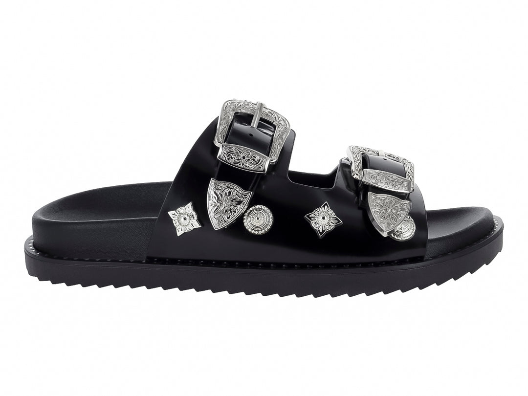 Sandalia negra para mujer con dos correas adornadas con hebillas y detalles ornamentales en color plata.