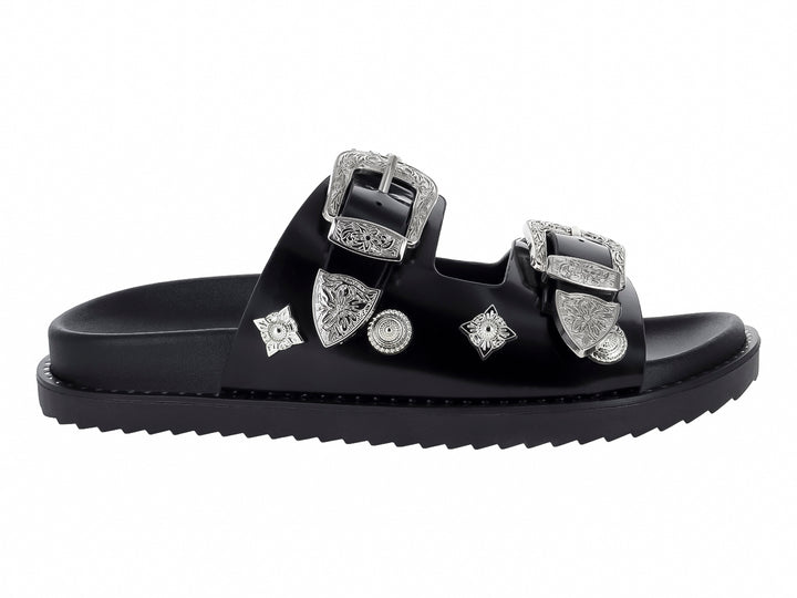 Sandalia negra para mujer con dos correas adornadas con hebillas y detalles ornamentales en color plata.