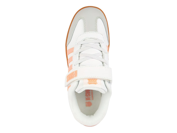 Tenis K-Swiss blancos con detalles en rosa y suela naranja, con cierre de velcro y agujetas para niños.