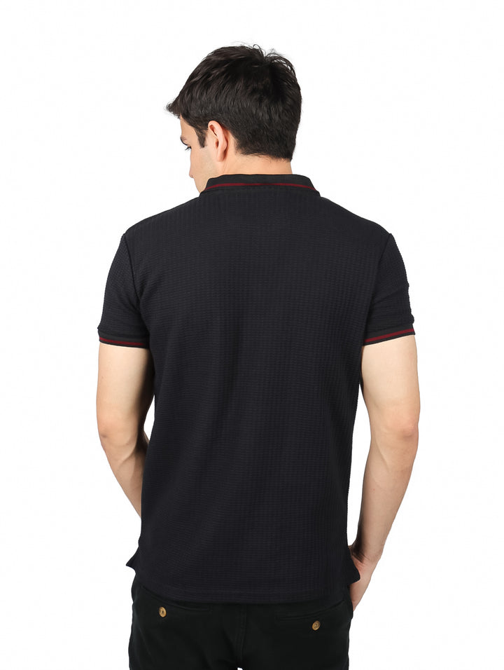 Hombre vistiendo playera polo color negro con detalles rojos en el cuello y mangas.