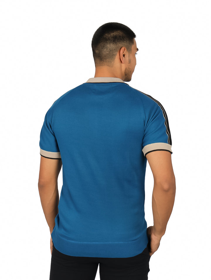 Hombre vistiendo playera polo azul con cuello beige, detalles en negro y cierre frontal.