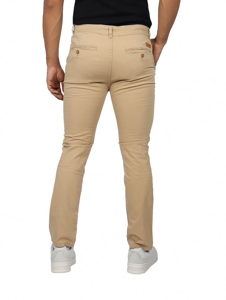 Hombre vistiendo un pantalón chino slim en color camel con calzado blanco sobre fondo blanco.