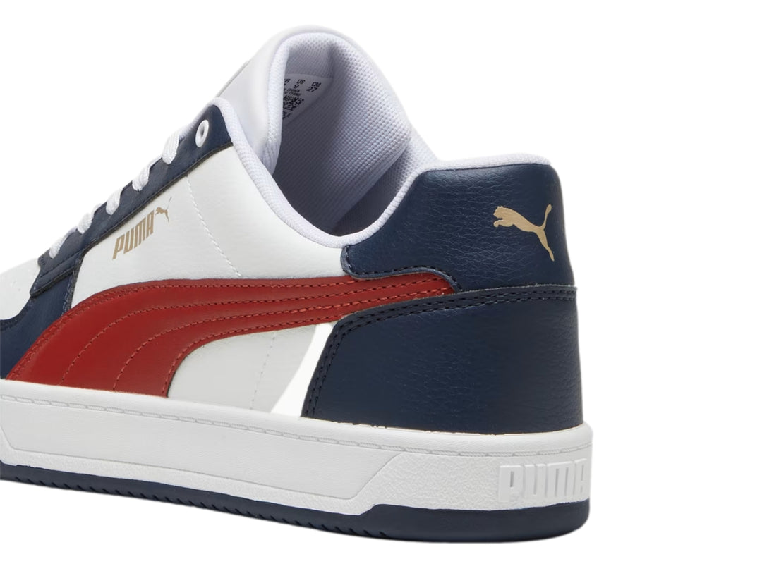 Tenis Puma Caven 2.0 color blanco con detalles en azul marino y franja roja lateral.